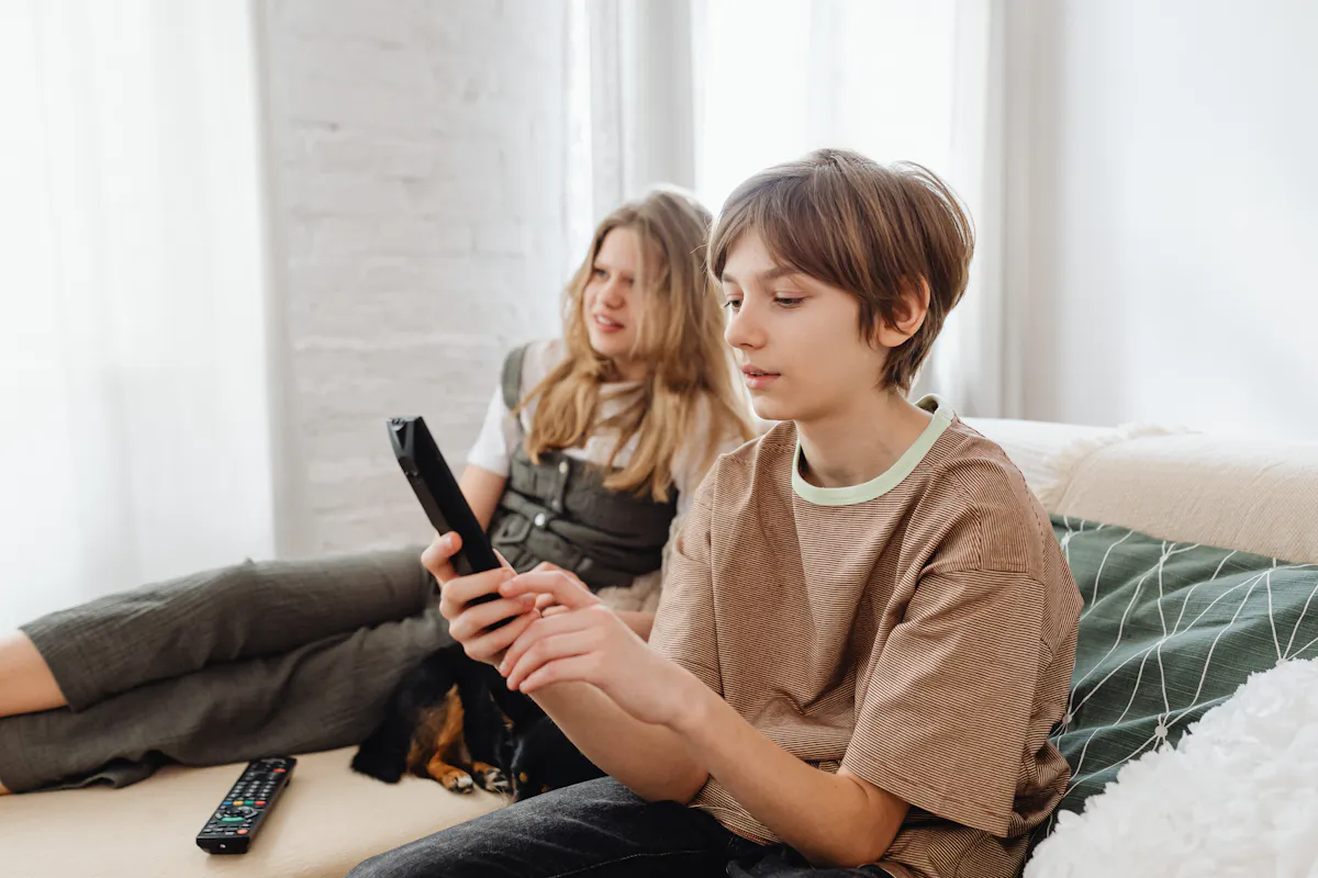 Two children holding a TV remote while sitting on a sofa